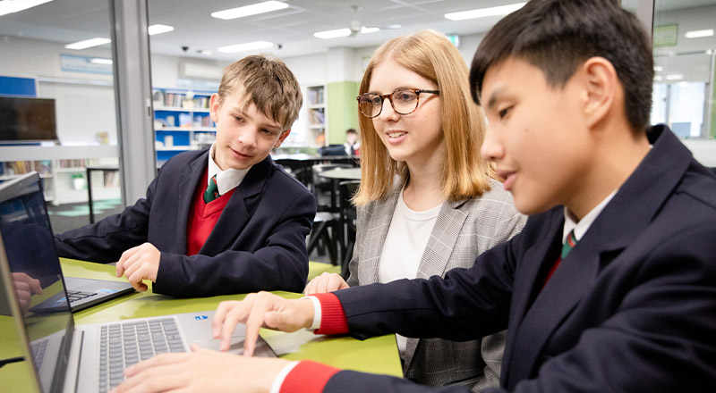 Teacher working with her students on a laptop at St John Paul II Catholic College Schofields and Nirimba