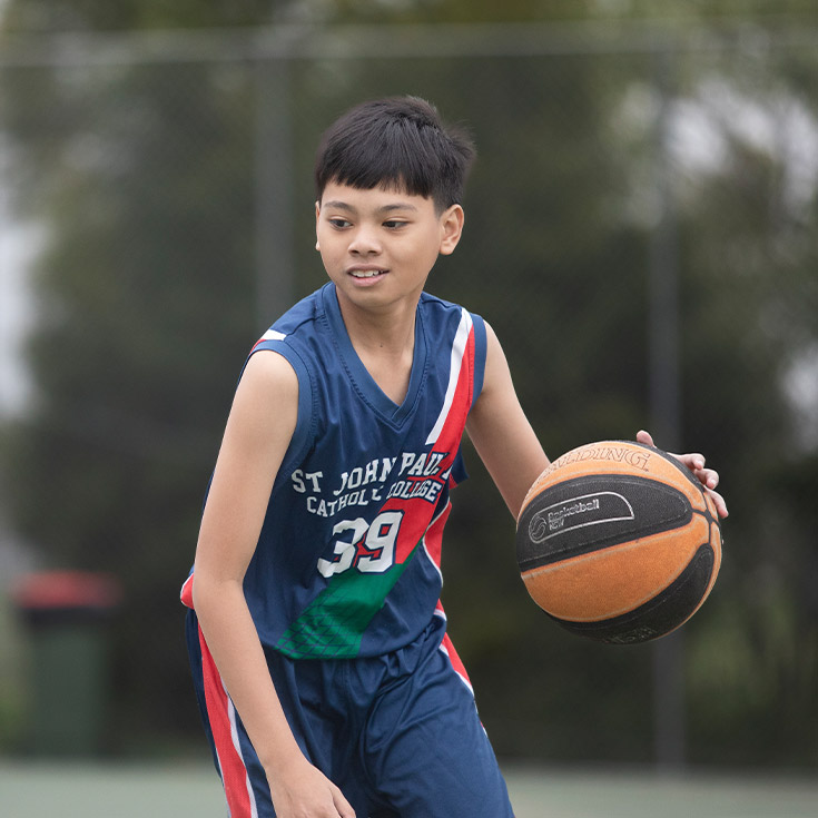 Student playing basketball on the basketball court at St John Paul II Catholic College Schofields and Nirimba